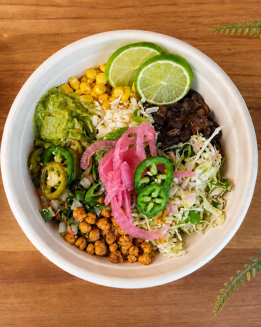 Colourful burrito bowl topped with lime, guacamole, pickled onions, and jalapeños